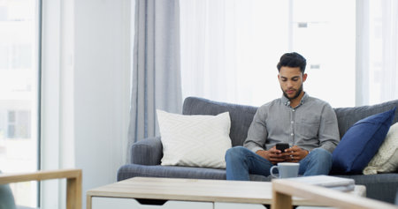Man, relax and morning with phone on sofa for online communication, texting or chatting at home. Male person, user or typing with mobile smartphone for connection, network or app on living room couchの写真素材