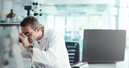Research, biotech or man in lab with microscope, vaccine test or medical experiment for cancer treatment. Cure, check or scientist with science report, study or sample with dna, bacteria and laptopの写真素材