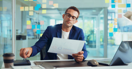 Businessman, documents and analysis with laptop for finance or company performance at office desk. Man, employee or analytics with paperwork for graph, chart or data on business growth at workplaceの写真素材