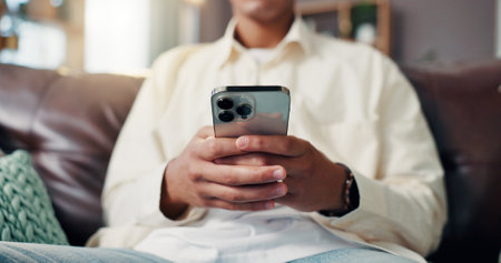 Phone, hands and man on sofa in home for social networking on mobile app for connection. Cellphone, communication and closeup of male person texting for online dating in living room at apartment.の写真素材