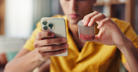 Medicine, hands and phone with pills search in home for medication information, health symptoms or question. Man, smartphone and mobile app for treatment, label instructions and prescription reminderの写真素材