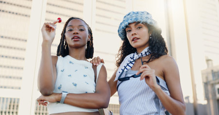 Streetwear, cool and women in city with fashion or lollipop for urban, edgy and trendy style together. Low angle, gen z friends and creative people in town for youth culture, unique outfit and swagの写真素材