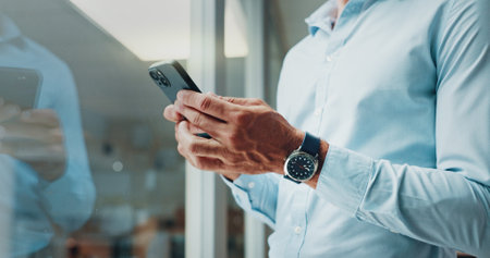 Hands, smartphone and texting by glass in office with reflection, contact and notification at startup. Business person, chat and click on mobile app, social media and networking at creative agencyの写真素材