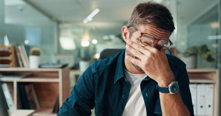 Man, night and tired journalist in office with fatigue, deadline and burnout for article or project. Overworked reporter, mistake or exhausted writer with eye strain for story editing or journalismの写真素材