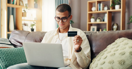 Credit card, laptop and man on sofa for online shopping, internet banking and payment in home. Ecommerce, fintech and person on computer for website sale, purchase and discount in living roomの写真素材