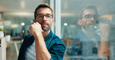 Reflection, thinking and business man in office for problem solving, decision and creative mindset. Planning, vision and serious worker with inspiration, idea and writer with pen by glass in startupの写真素材