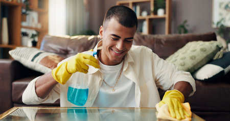 Happy man, cleaning and surface with detergent for housekeeping, disinfection or hygiene at home. Male person, maid or cleaner with smile, gloves or spray bottle for bacteria or germ removal at houseの写真素材