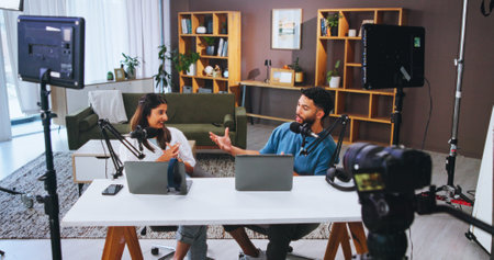 Conversation, laptop and podcast with people in home living room for live broadcast or recording. Camera, microphone or streaming with man and woman influencer in apartment for subscription serviceの写真素材