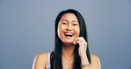 Asian woman, portrait and laughing in studio for joke, funny memory and comedy with mockup space. Model, female person and happiness with humor by blue background, satisfaction and emoji reactionの写真素材