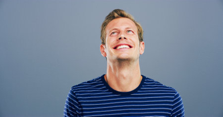 Smile, space and thinking with man in studio for contemplation, memories or nostalgia. Idea, inspiration and mockup with happy model isolated on gray background for future, planning or visionの写真素材