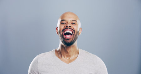 Comedy, man and portrait for laugh in studio with confidence, joke or good mood on gray background. Space, excited model and smile with carefree personality for comic, humor or funny reaction to memeの写真素材