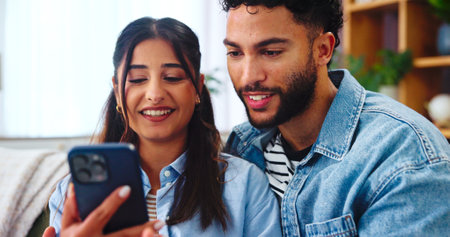 Couple, smartphone and social media on sofa with hug, bonding and funny story in home. Woman, man and phone in living room for storytelling, comedy and celebrity news on timeline with internet gossipの写真素材