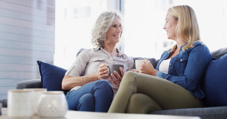 Home, senior mother and daughter with conversation, relax and bonding together in living room. Family, parent and women on couch, discussion or comfort with weekend break, reunion or coffee in loungeの写真素材