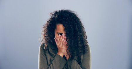 Crying, sad and woman in studio, sorrow and emotional reaction on blue background. Person, model and depression with stress, shame or grief with loss, mourning and broken heart with breakup or traumaの写真素材
