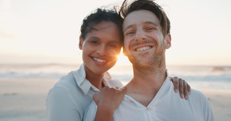 Couple, sunset and smile at beach on holiday, summer vacation and travel together. Ocean, man and woman embrace outdoor for romantic date, love and portrait for interracial relationship with spaceの写真素材
