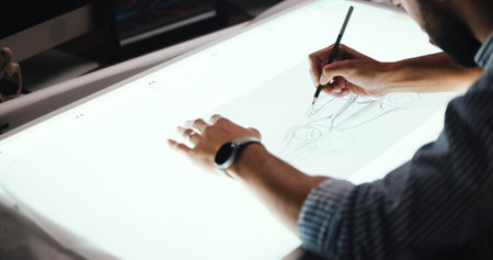Man, hands and designer with drawing for car prototype, modeling or graphic design on light table. Male person, mechanical engineer or digital sketch with 2D vehicle, blueprint or automobile projectの写真素材