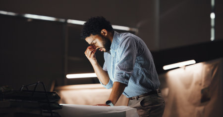 Frustrated man, architect and night with headache for overworked stress or mistake at office. Businessman, civil engineer or designer with migraine or eye strain for project deadline or pressureの写真素材