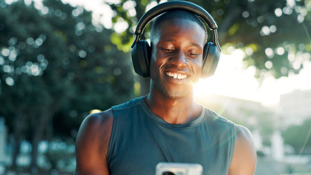 Fitness, headphones and black man on mobile for music, streaming hip hop or sound. Happy athlete, phone and listening to radio outdoor for exercise podcast, audio or motivation playlist on internetの写真素材