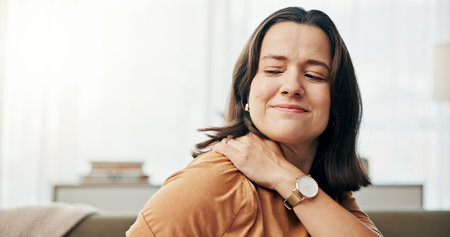 Shoulder pain, injury and woman on sofa in home with stress, muscle tension and joint ache in living...