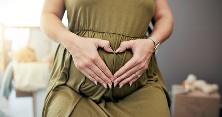 Pregnant, woman and heart hands on stomach in home for baby nesting, prenatal care and connection in nursery. New mother, person and love emoji on tummy for pregnancy wellness, affection or maternityの写真素材