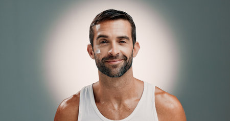 Skincare, face cream and portrait of man in studio for wellness, health and hydration for facial treatment. Dermatology, beauty and person with lotion, moisturizer or cosmetics on gradient backgroundの写真素材