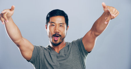 Portrait, cheering and man in studio, sign and celebration with confidence on gray background. Asian person, pride and model with symbol, icon and happiness with support, success and achievementの写真素材