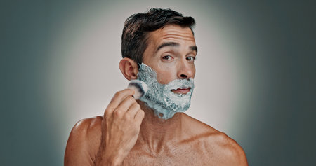 Shaving, cream and grooming with portrait of man in studio for beard, beauty and cleaning. Hair removal foam, cosmetics and self care with person and brush on background for hygiene and skincareの写真素材