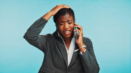 Phone call, upset and black woman in studio, business and conversation on blue background. African person, consultant and model with cellphone, bad news and failure with mistake, stress or frustratedの写真素材