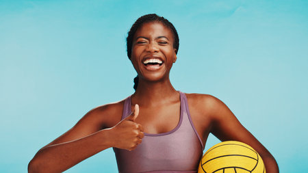 Thumbs up, ball and portrait of black woman in studio for workout, exercise and training for volleyball. Happy, fitness and person with emoji for yes, like and approve for sports on blue backgroundの写真素材