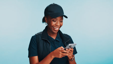 Black woman, phone and happy in smile for delivery, customer service and company review on internet. Courier person, smartphone and online on blue background for client contact, logistics or scheduleの写真素材