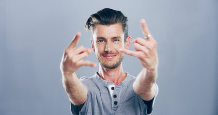 Rock, hands and portrait of man in studio with gesture for emoji, heavy metal and edgy attitude. Mockup space, rebel and face of person with punk sign, symbol and devil horns on gray backgroundの写真素材