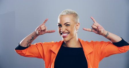 Portrait, edgy or happy woman with rock hand gesture in studio for expression or space on gray background. Culture, cool female rocker and crazy model with devil horn sign, funky emoji or punk symbolの写真素材
