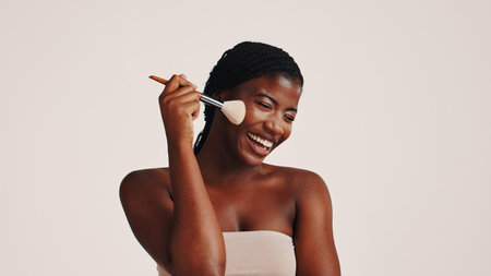 Brush, happy and black woman in studio with makeup, beauty or cosmetics for getting ready. Smile, cosmetology and African female person with blush for facial color or glow by white background.の写真素材