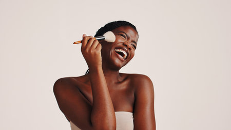Brush, laughing and black woman in studio with makeup, beauty or cosmetics for getting ready. Happy, cosmetology and African female person with blush for facial color or glow by white background.の写真素材