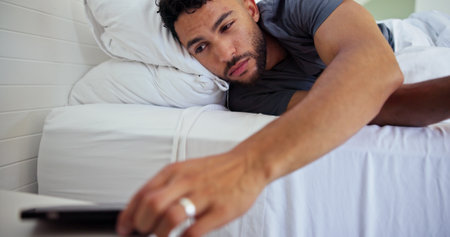 Man, bed and wake up with phone alarm for morning routine, start day and sound alert in home. Sleepy, person and mobile notification in bedroom to get up, lazy weekend and awake with smartphone appの写真素材