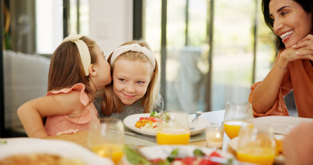 Children, food and girl with gossip whisper at lunch for sibling secret, mystery news or mother listening. Family, people and sister share private story in home for trust and confidential informationの写真素材