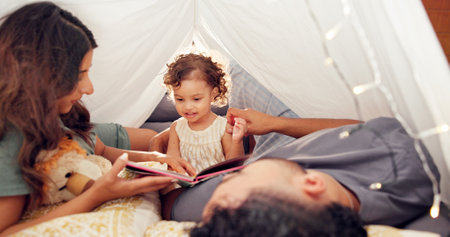 Tent, parents and reading with baby in home for bonding together, story time and connection with trust. Book, people and fun activity with child in blanket fort for happy relationship, love or careの写真素材