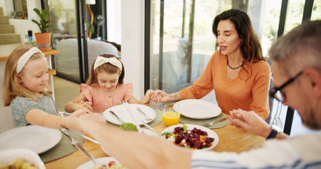 Praying, lunch and family at dining table in house for healthy, wellness and nutrition meal together. Gratitude, worship and parents with children for food with holding hands, religion and bonding.の写真素材