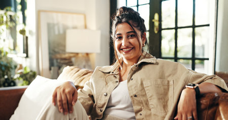 Portrait, relax and happy woman in home on sofa for peace, calm or break on staycation with confidence in house. Face, smile and person in living room for chill, rest or comfort in apartment in Dubaiの写真素材