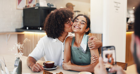 Couple, happy and kiss in picture in restaurant for coffee date memory, relationship support and social media post. Gen z people, smile and photography in cafe for bonding, romance and connectionの写真素材