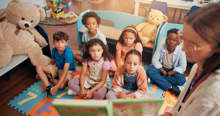 Reading book, classroom and children listening to teacher for lesson, education and learning. Preschool, students and kids on floor with educator for storytelling, language development and knowledgeの写真素材