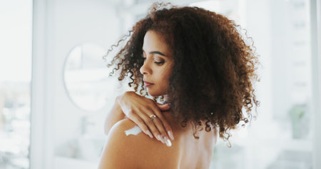 African woman, lotion and shoulder in home, bathroom and moisturizer application for skin wellness. Person, cream and product with vitamin E, results and benefits with self care routine at apartmentの写真素材