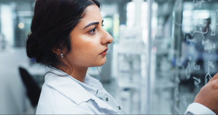 Glass wall, science and writing with woman in laboratory for equation, formula or solution. Healthcare, innovation and medical with person at work on clinical trial for pharmaceutical researchの写真素材