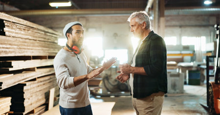 Collaboration, planning and talking with carpenter men in workshop for manufacturing or production. Carpentry, industry and teamwork with woodworking people in factory together for conversationの写真素材