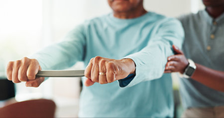 Resistance band, physical therapy and hands of man in clinic for consultation with muscle recovery. Injury, healthcare and woman physiotherapist for helping mature patient with stretch arm exerciseの写真素材