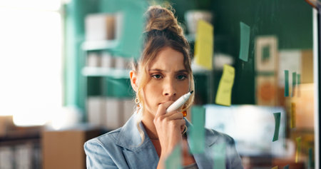 Glass wall, logistics and thinking with woman in office for delivery or shipping schedule. Planning, problem solving and supply chain with serious person in depot or warehouse for ecommerce trackingの写真素材