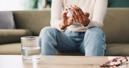 Person, hands and pills with water on sofa for prescription, medication or side effects at home. Closeup, patient or user with pharmaceuticals tablets for illness, symptoms or virus on couch at houseの写真素材