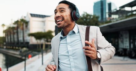 Businessman, happy and dancing outdoor with headphones for morning commute, audio playlist or streaming music. Professional, person and walking in city with sound track, radio and travel to new jobの写真素材