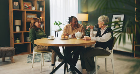 Elderly, women and retirement with eating in home with conversation, bonding or wellness with tea party. Senior, people and friends in hospice with talking for relax, support or happy at dinner tableの写真素材