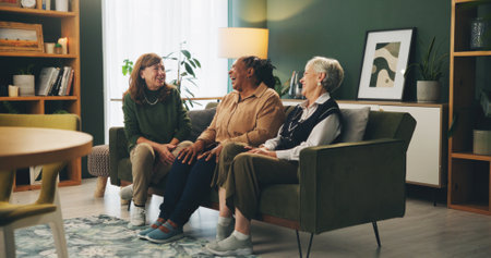 Senior women, friends and laugh on sofa with funny story, memory or gossip with bonding in retirement. People, relax and conversation with smile, care or connection on couch in lounge at nursing homeの写真素材